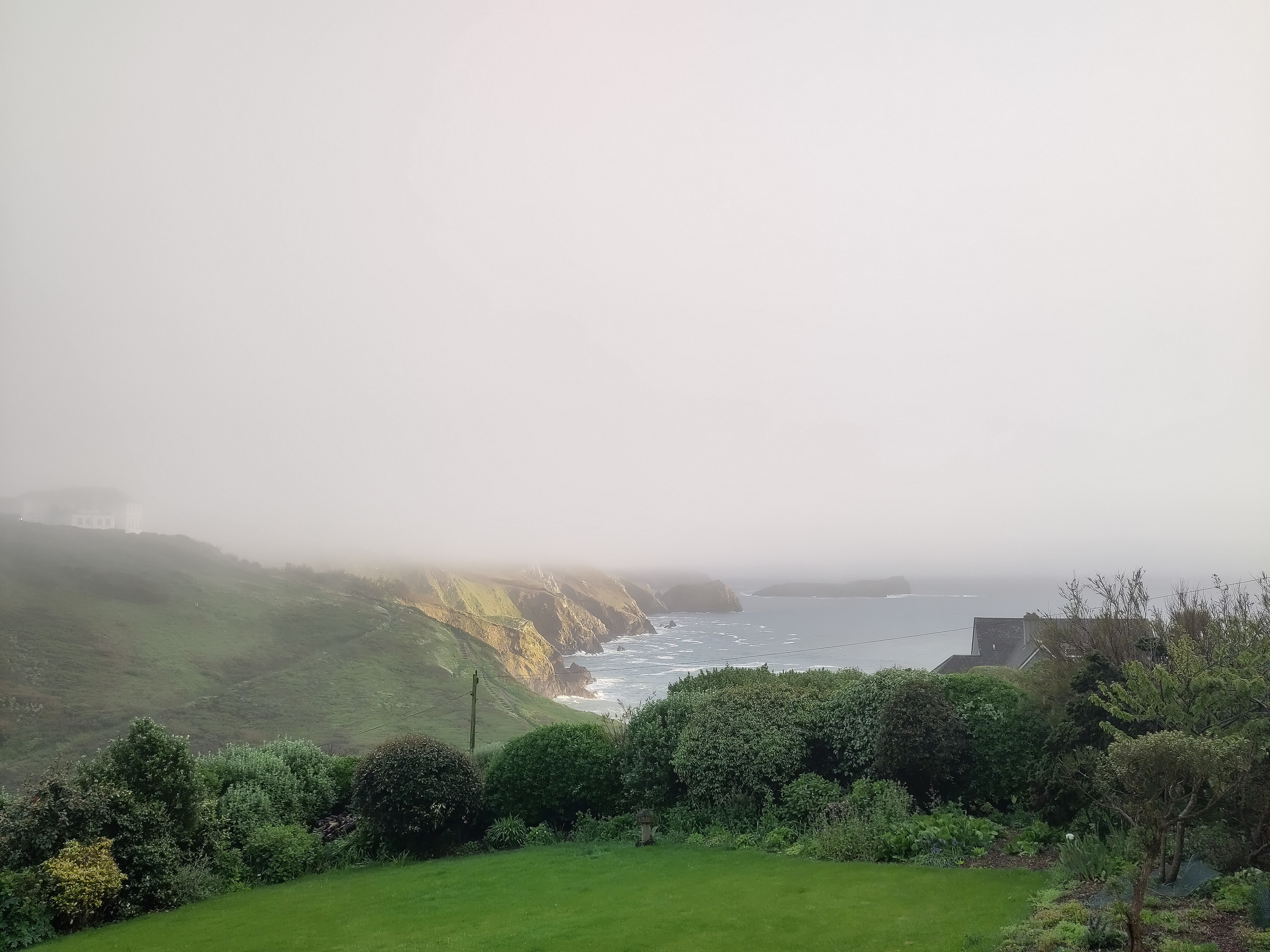 a photo of the sea and a small stretch of coastline bathed in sunlight, with the top half of the frame blank white fog