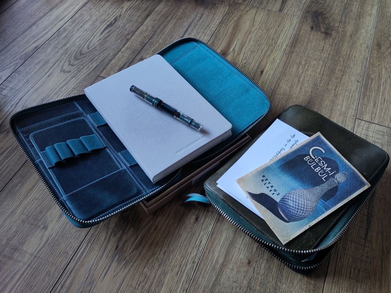 galen leather a5 zipfolio okyanus mavi a blue leather notebook cover, a grey linen-covered notebook, a fountain pen, and some decorative bits and pieces